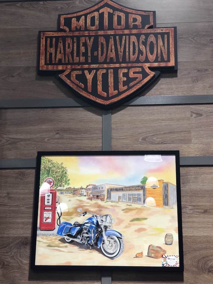 Tableau d'une Harley-Davidson bleue dessinée et accroché sous le logo de la marque de moto américaine